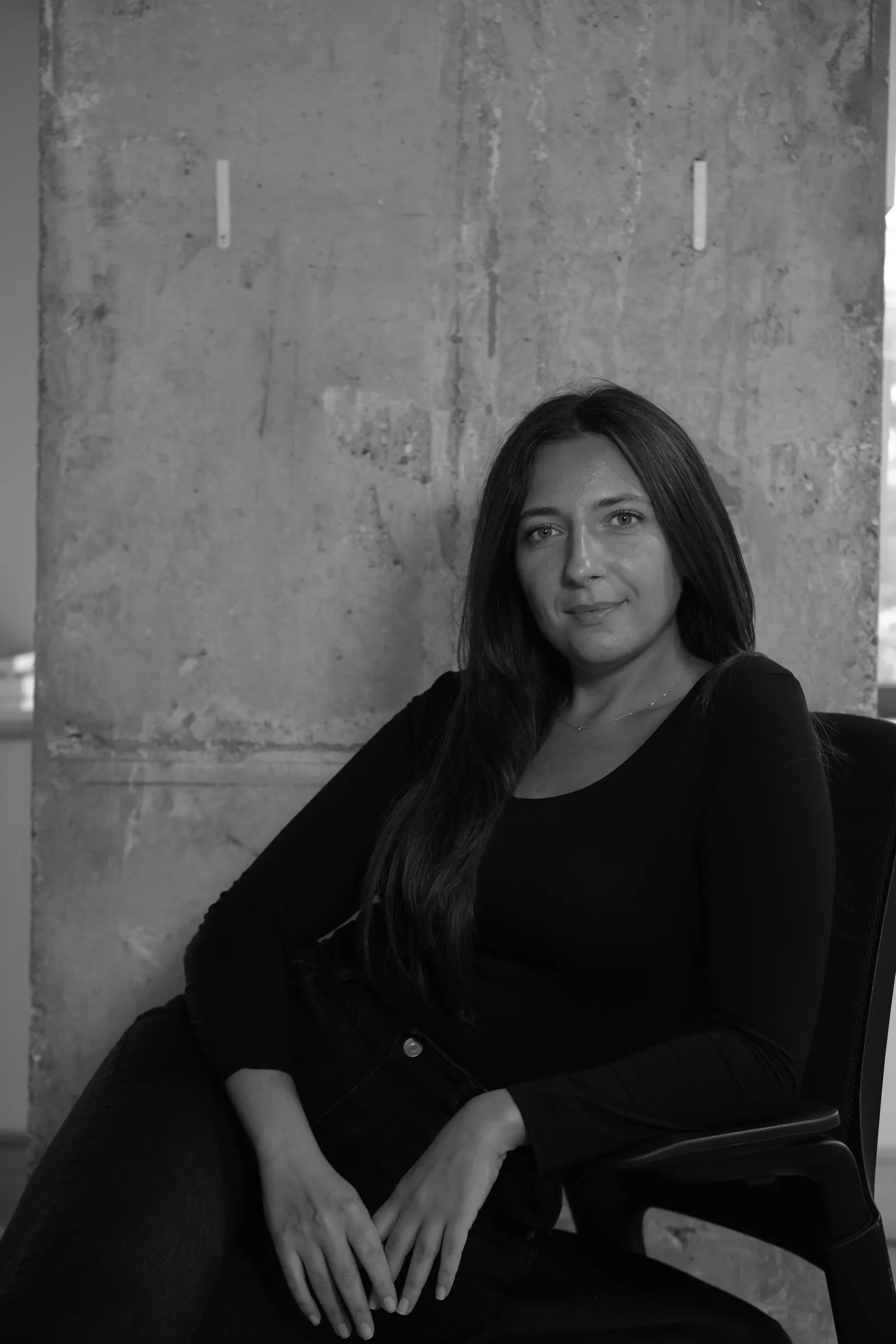 Black and white portrait of a woman seated in front of a concrete wall
